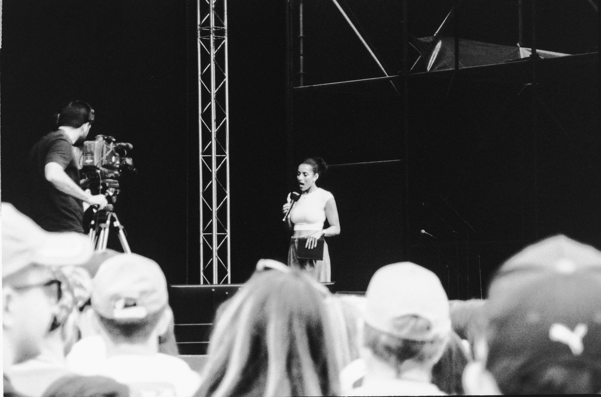 A presenter speaking on stage while a television camera films from the audience.